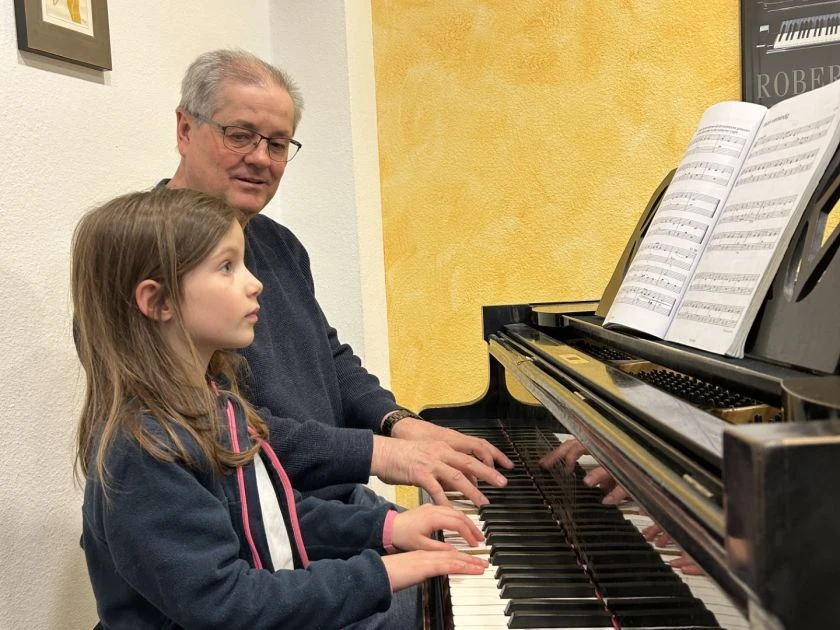Pro Musica Mädchen spielt Klavier, Lehrer unterstützt beim Schnupperunterricht in der Musikschule