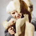 Louise Stomps at work on her last sculpture "Der Aussteiger", Rechtmehring 1987 Elderly person working intently with a mallet and chisel on a rough wooden sculpture.