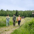 6. neanderland WANDERWOCHE Wandernde Personen auf einem Feldweg im neanderland mit Wald und Hochsitz.