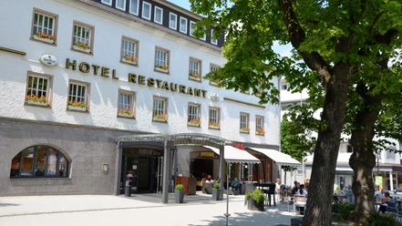 Restaurant_Ratskeller_SZ-Bad_HD_16zu9.JPG Weißes Gebäude des Hotels Ratskeller mit Außengastronomie unter Bäumen.