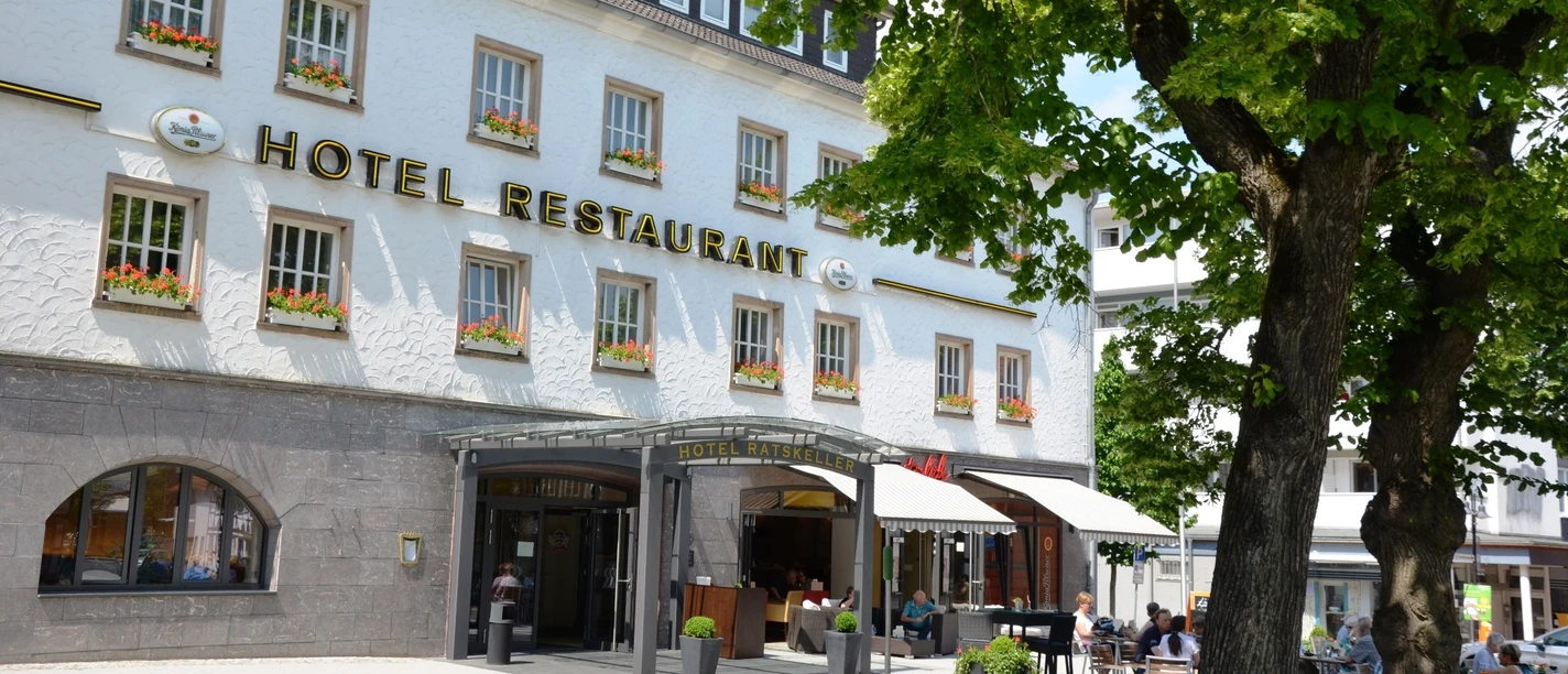 Restaurant_Ratskeller_SZ-Bad_HD_16zu9.JPG Weißes Gebäude des Hotels Ratskeller mit Außengastronomie unter Bäumen.