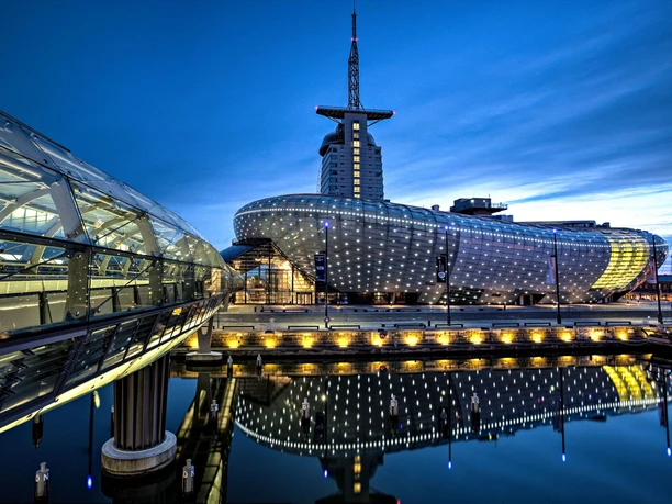 Klimahaus Bremerhaven Außenansicht 3000 px(c) Ralph Langer_WEB.jpg Beleuchtetes Klimahaus bei Nacht, zu dem die gläserne Havenbrücken führt