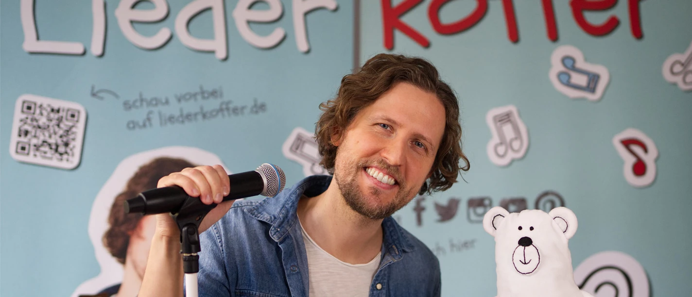 Liederkoffer Frank Lemke in Büsum Ein Mann lächelnd an einem Mikrofonständer neben einem kleinen Plüscheisbären.