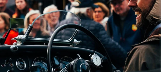 Kaiser Karl Classic (c) MSC Aachen.jpg Nahaufnahme des Innenraums eines Oldtimers, in dem ein Mann lächelnd sitzt. Vor dem Wagen stehen einige Zuschauer*innen.