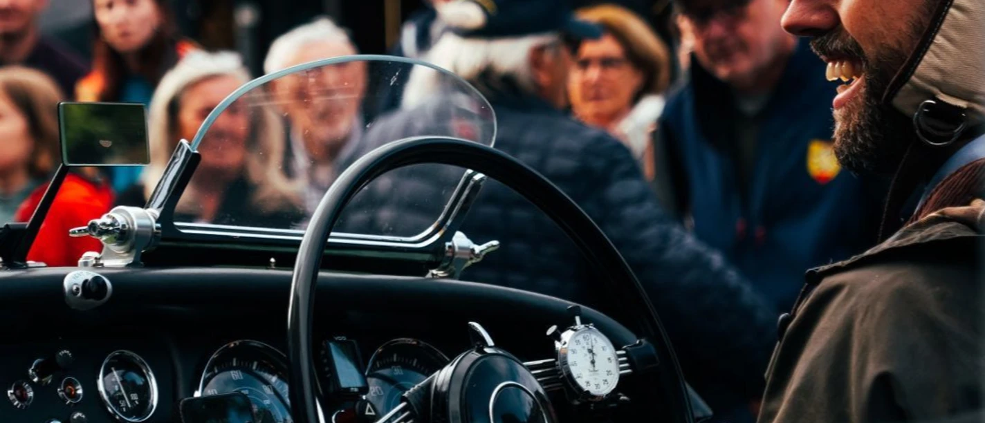 Kaiser Karl Classic (c) MSC Aachen.jpg Nahaufnahme des Innenraums eines Oldtimers, in dem ein Mann lächelnd sitzt. Vor dem Wagen stehen einige Zuschauer*innen.