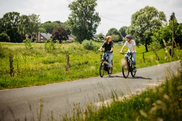 Reizen tussen weilanden en verre uitzichten Twee fietsers op een rustige landweg op het platteland van Osnabrück, omringd door weilanden, bomen en een landelijke omgeving.