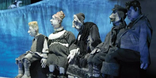Fünf unterschiedliche Figuren eines Figurentheaterstücks sitzen nebeneinander auf einer Bank und schauen nach links.
