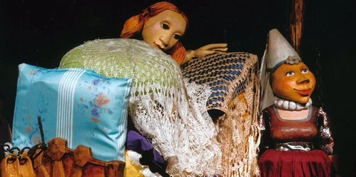 Die Prinzessin auf der Erbse (c) KOBALT Figurentheater Lübeck.jpg Eine Figur eines Figurentheaterstücks liegt in einem Bett aus vielen Matratzen und eine andere steht davor.