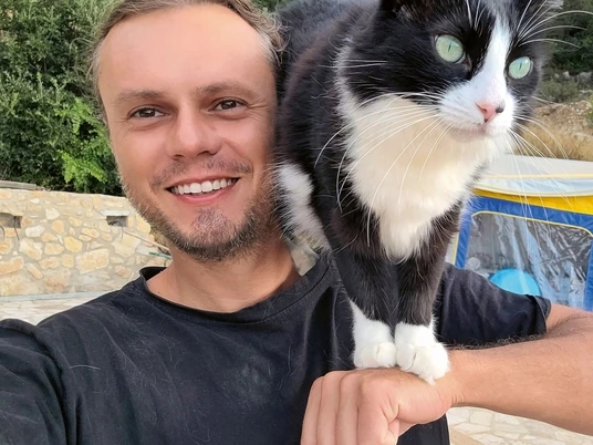 Mit der Katze weiter um die Welt_Lesung (c) Martin Klauka.jpg Ein junger Mann macht lächelnd ein Selfie mit seiner schwarz-weißen Katze, die auf seinem Arm sitzt.