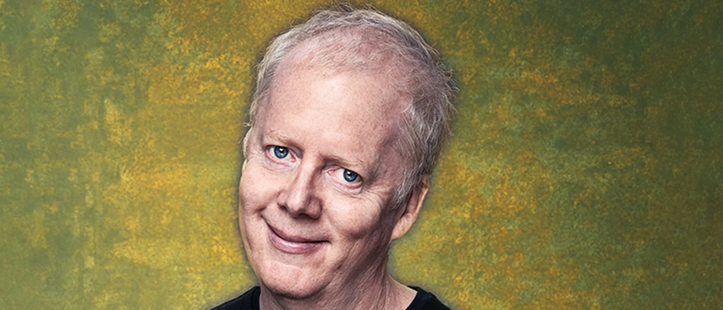 John Doyle Man with microphone in front of yellow-green background with a slight smile