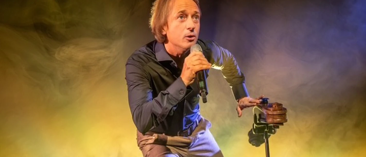 Person on stage with microphone in hand, in front of a background of yellow and blue light.