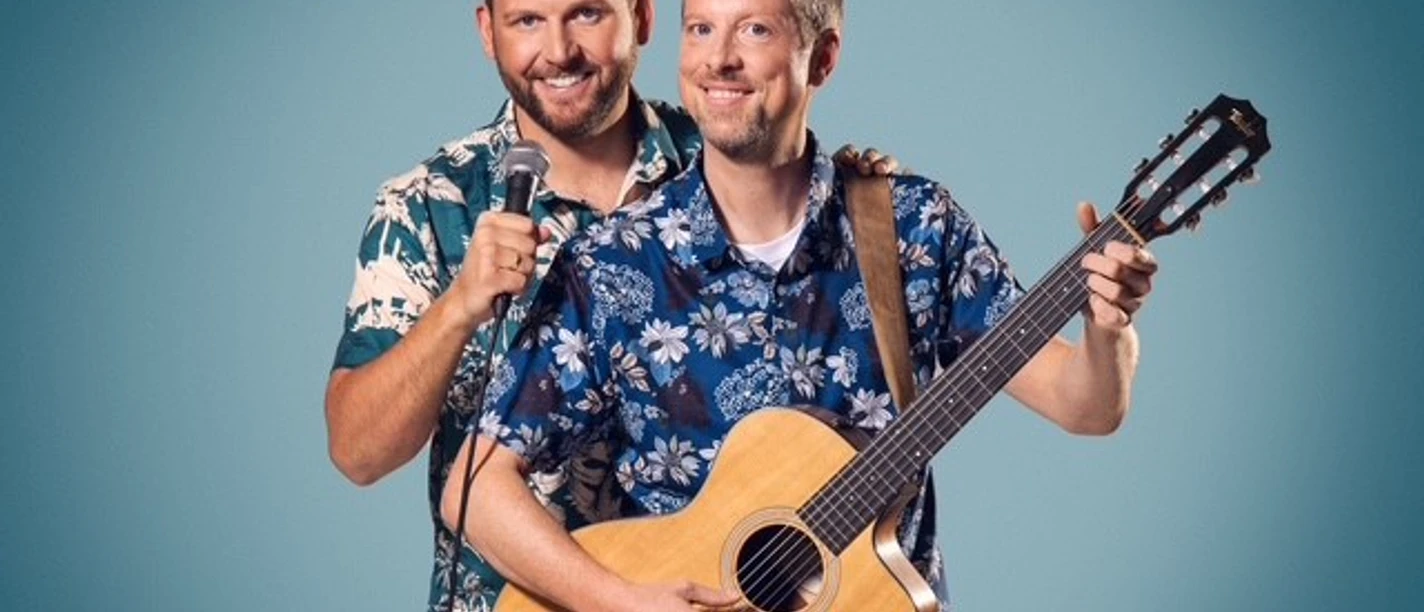 Two men in Hawaiian shirts, one with a guitar, the other with a microphone, against a blue background.
