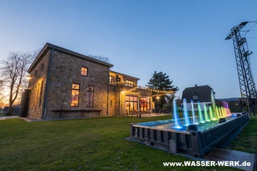 Wassershow am Wasserwerk Tecklenburg.jpg Beleuchtete Wassershow vor altem Wasserwerk in Tecklenburg bei Abenddämmerung