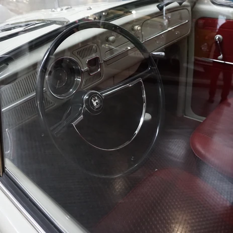 Automuseum - Lenkrad.JPG Blick in einen weißen VW Käfer mit großem Lenkrad und roten Sitzen.