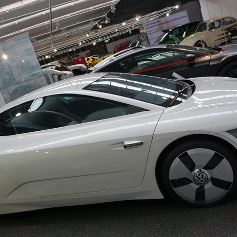 Automuseum - Zukunftsauto.JPG Weißes, futuristisches Volkswagen-Konzeptfahrzeug in einer Ausstellungshalle, seitlich aufgenommen, mit aerodynamischem Design und glatten Linien; im Hintergrund weitere Sportwagen