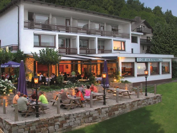 Außenansicht Hotel mit Terrasse und Biergarten, Gäste an Holztischen, umgeben von Wald und Wiesen.