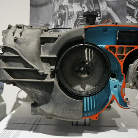 Automuseum - Motor 1.JPG Schnittmodell eines Automotors mit grauem Gehäuse und blau-orange markiertem Innenleben.