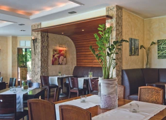 Hotel-Restaurant Am Rosenberg Restaurantbereich mit Holztischen, gepolsterten Bänken und Pflanzen im Innenraum.