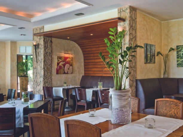 Hotel-Restaurant Am Rosenberg Restaurantbereich mit Holztischen, gepolsterten Bänken und Pflanzen im Innenraum.