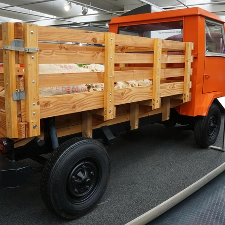 Automuseum - Transporter.JPG Orangefarbener historischer VW-Transporter mit Holzpritsche und Jutesäcken in Museumshalle.