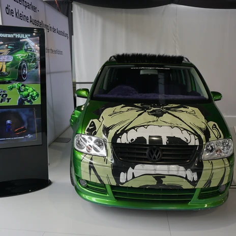 Automuseum - Hulk-Touran.JPG Grüner VW Touran mit großem Hulk-Gesicht auf der Motorhaube neben einer Infostele im Museum.