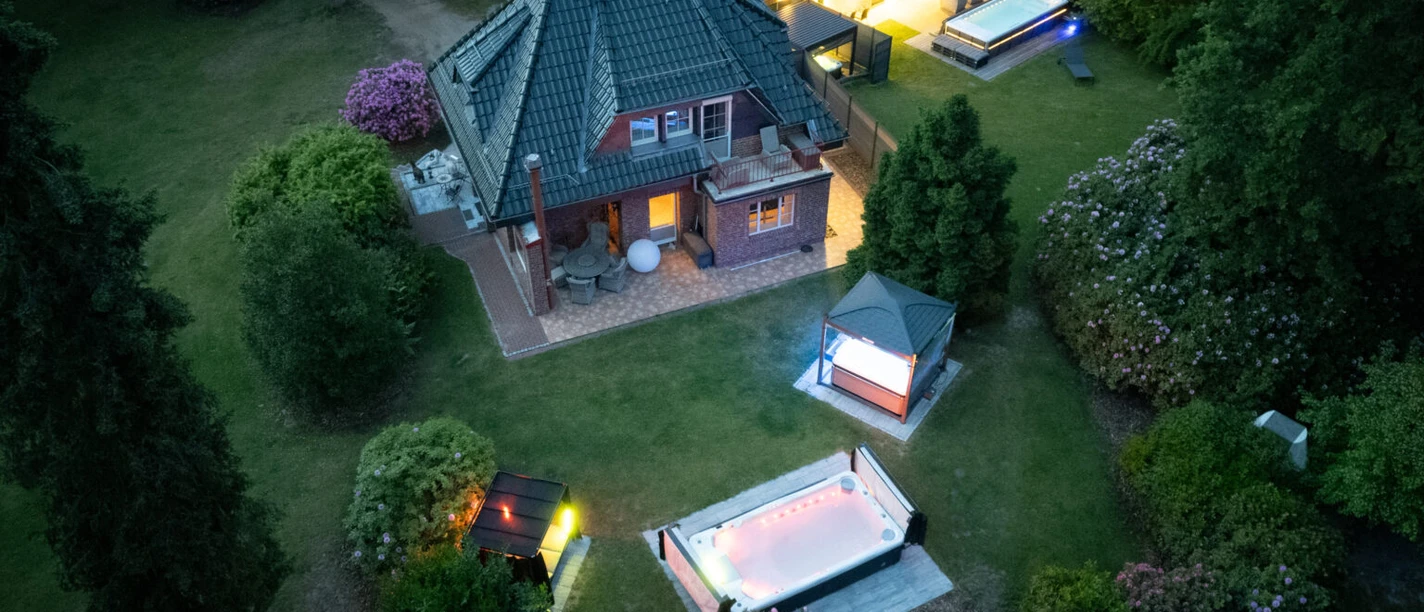 Royal Whirlpool Suites Lüneburger Heide Luftaufnahme der Whirlpool Suites in Rehlingen mit beleuchteten Außenpools und Garten bei Dämmerung.
