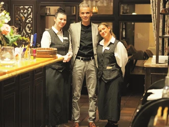 Restaurantchef Daniel Richau mit seinem Team Restaurantchef Daniel Richau steht mit zwei Servicekräften im Gastraum.