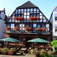 Zum Braunen Hirschen - Außenansicht Fachwerkhaus mit Blumenbalkonen und Außenterrasse mit grünen Sonnenschirmen.