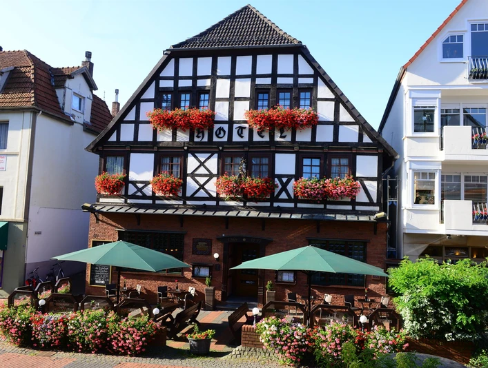 Zum Braunen Hirschen - Außenansicht Fachwerkhaus mit Blumenbalkonen und Außenterrasse mit grünen Sonnenschirmen.
