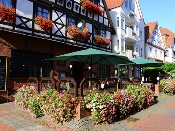 Zum Braunen Hirschen - Außengastronomie. Außenterrasse mit grünen Sonnenschirmen vor Fachwerkhaus, umgeben von Blumen.