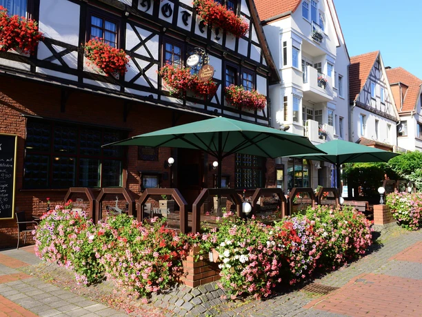 Zum Braunen Hirschen - Außengastronomie. Außenterrasse mit grünen Sonnenschirmen vor Fachwerkhaus, umgeben von Blumen.