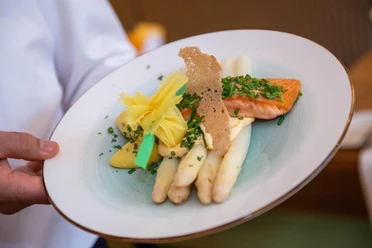 Regionale Spezialitäten Teller mit weißem Spargel, Lachsfilet, Sauce und frischen Kräutern angerichtet.