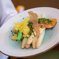 Regionale Spezialitäten Teller mit weißem Spargel, Lachsfilet, Sauce und frischen Kräutern angerichtet.