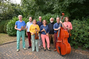 Jazzband Blue Baroque Sieben Musiker:innen des Ensembles Blue Barock posieren mit ihren Instrumenten vor grünen Büschen.