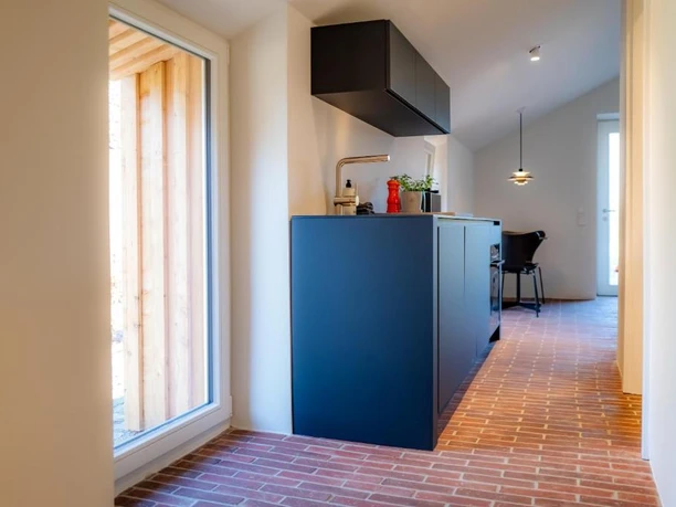 Innnenansichten Moderne Küchenzeile mit dunklen Fronten, Backsteinboden und Essplatz am Fenster.