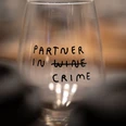 Wein & Crime Weinglas mit Aufschrift "Partner in Wine Crime", wobei "Wine" durchgestrichen ist.