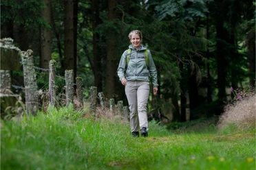 Kerstin Rubel Kerstin Rubel wandert lächelnd mit Rucksack auf einem grünen Waldweg in Wipperfürth.