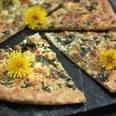 Wanderung mit Brunch Frühlings-Fladenbrot mit Kräutern und Käse, dekoriert mit gelben Löwenzahnblüten.