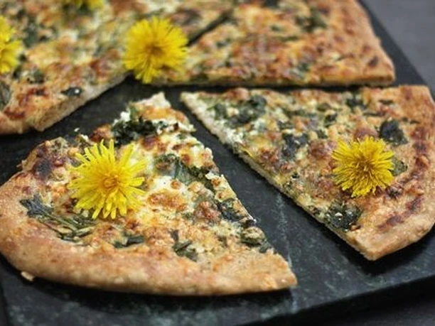 Wanderung mit Brunch Frühlings-Fladenbrot mit Kräutern und Käse, dekoriert mit gelben Löwenzahnblüten.