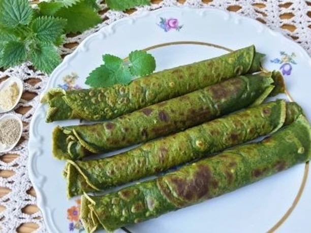 Early bird walk und Brunch Grüne, gerollte Pfannkuchen auf einem floralen Teller, umgeben von Brennnesselblättern und Gewürzpulver.