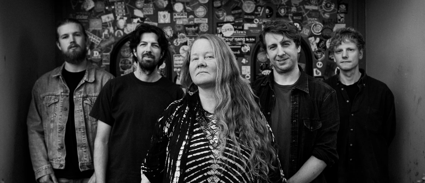 Layla-Zoe Layla Zoe mit Band vor beklebter Clubwand, schwarzweißes Porträt