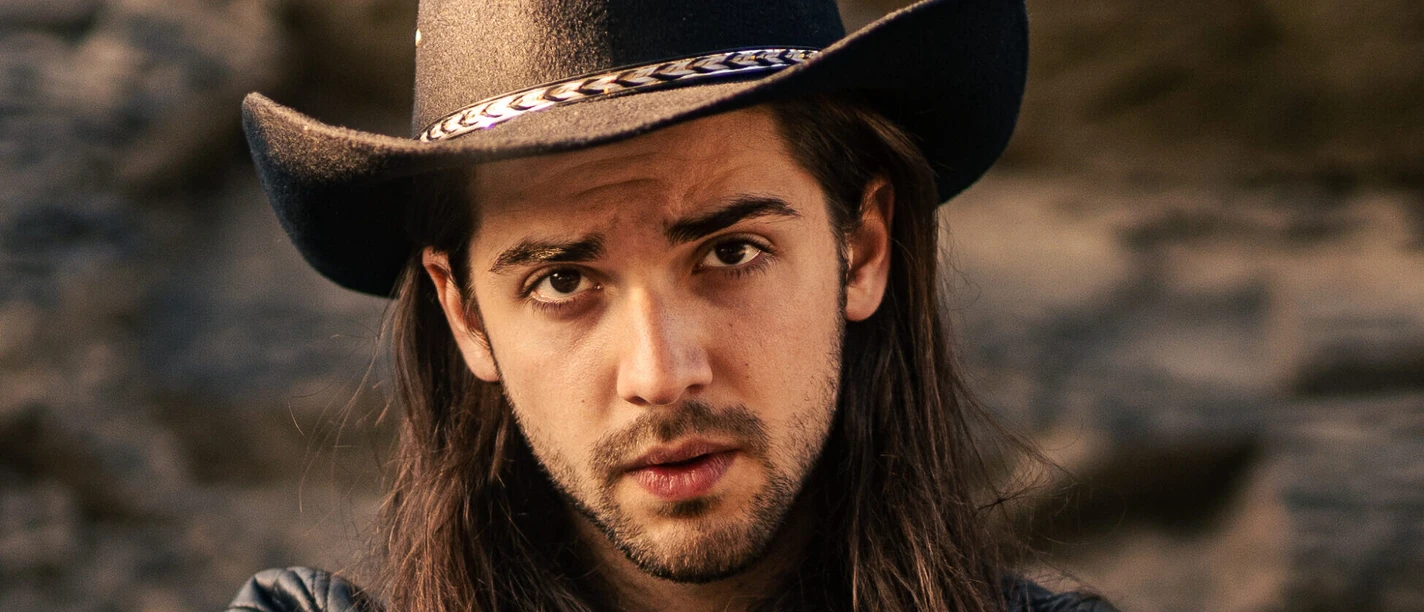 DAVID TARAKONA Porträt von David Tarakona mit schwarzem Cowboyhut und Lederjacke vor Felswand