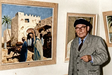 Smalian-gross-2026-KI-color.jpg Maler Paul Smalian mit Brille und Baskenmütze neben seinen orientalischen Gemälden.