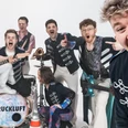 Eine mehrköpfige Band mit ihren Instrumenten schaut lachend in die Kamera.