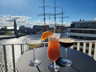 Cocktails auf einem Stehtisch in einer Dachterrassen-Bar mit Blick auf einen Windjammer im Hafen