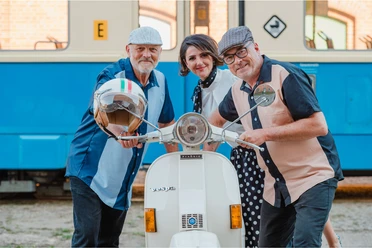 Polkadot und die Riminis in Büsum Zwei Männer und eine Frau stehen an einer Vespa und schauen in die Kamera.