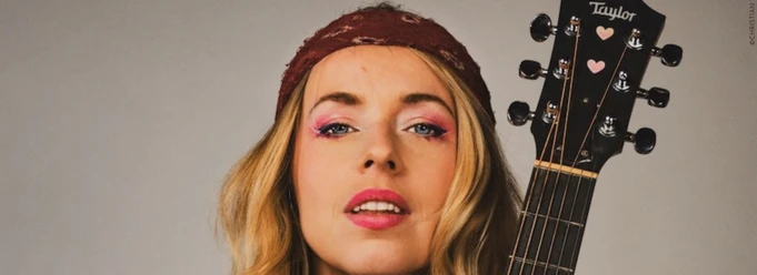 Miss Allie_Burg Wilhelmstein (c) Christian Verch.jpg Eine junge Frau hält eine Gitarre in der Hand und schaut mit selbstbewusstem Blick in die Kamera.
