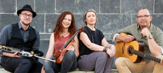 CARA Eine vierköpfige Band sitzt lässig mit ihren Instrumenten vor einer grauen Mauer.