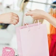 Eine rosafarbene Einkaufstüte wird von einer Hand in eine andere gereicht.