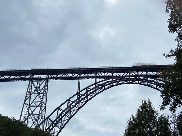 Müngstener Brücke Historische Stahlbogenbrücke mit Dampfzug überquert die Landschaft in Solingen unter bewölktem Himmel.